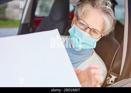 Ältere Frauen mit Gesichtsmaske im Auto erhalten Informationen zu Coronavirus als Broschüre auf einem Blatt Papier zu Covid-19 Stockfoto