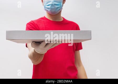 Mann vom Lieferservice in rotem T-Shirt mit Schutzmaske und Handschuhen mit Pizza-Box. Stockfoto