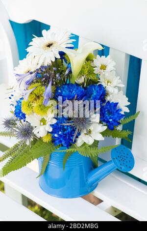 Bunte Blumen in einer kleinen Gießkanne auf einer Gartenbank Stockfoto