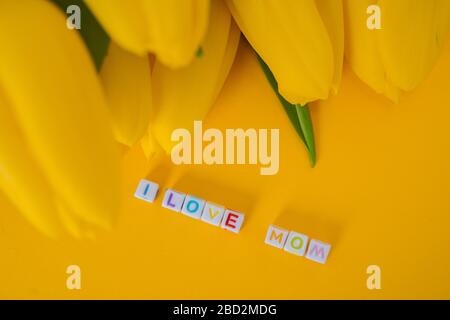 Muttertag Grußkonzept. MAMA Text mit gelben Tulpen Blumen. Fröhlicher Hintergrund für den Muttertag. Stilvolles flaches Lay mit Blumen und Platz für Text. g Stockfoto