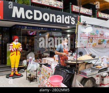 Bangkok, Thailand - 27. Februar 2020: Ein traditioneller thailändischer Straßennahrungsmittelanbieter vor einer lokalen McDonald's Fast-Food-Filiale. Stockfoto