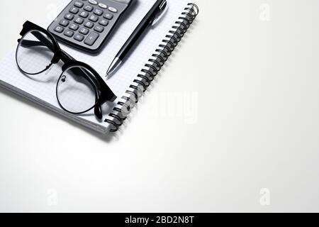 Weißer Bürotisch mit Notizblock, Brille, Taschenrechner und anderem Zubehör. Draufsicht, flacher Lay. Arbeiten Sie von zu Hause aus. Lernen Sie von zu Hause aus Stockfoto