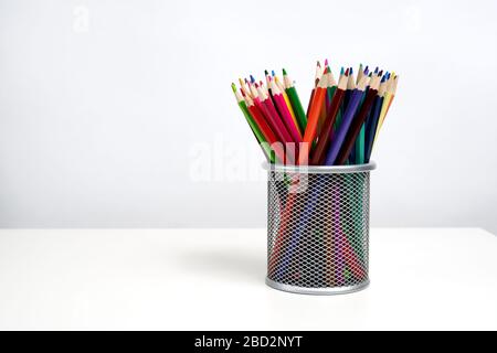 Verschiedene Farbstifte in silbernem Bürobecher auf weißem Tisch und weißem Hintergrund. Schule. Kinder. Stockfoto