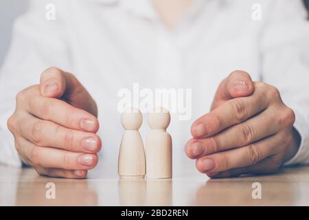 Familienversicherungskonzept - Hände schützen abstrakt zwei Holzleute. Nahaufnahme. Stockfoto