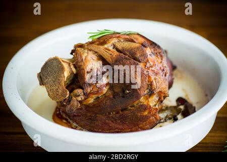 Gebackener Schweineschank mit Gewürzen in Keramikform, auf einem Holztisch Stockfoto