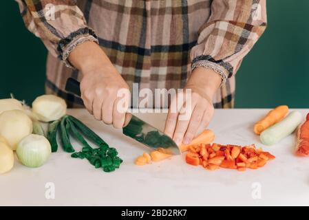 Frau schneidet frische Karotte in ihrer Küche auf weißem Marmor, um ihr Essen zuzubereiten. Stockfoto