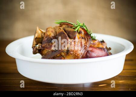 Gebackener Schweineschank mit Gewürzen in Keramikform, auf einem Holztisch Stockfoto