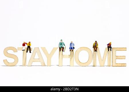 Konzeptionelles Bild der Miniaturfigur Menschen saßen auf einem Holzschild, in dem sie die Wörter ausgeschrieben haben, bleiben zu Hause Stockfoto