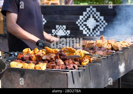 Mann in schwarzem T-Shirt, das mariniertes Fleisch auf dem Grill braten lässt. Straßenküche und Kochkonzept für den Außenbereich Stockfoto