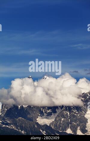 Hohe Felsenberge mit Schnee und Gletscher, versteckt in Wolken und blauem bewölktem Himmel. Kaukasusgebirge. Georgia, Region Svanetia, Mount Ushba im Sommer. Stockfoto