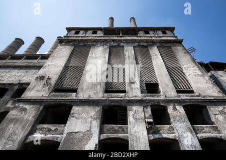 Symmetrische Weitwinkelansicht von unten an der Fassade einer alten Betonfabrik in Norditalien, gegen einen massiven blauen Himmel Stockfoto