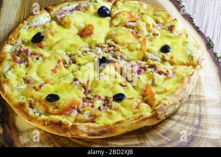 Pizza in Scheiben mit Wurst, Speck, Oliven und Tomaten ist auf einem Holztisch. Fast Food Stockfoto