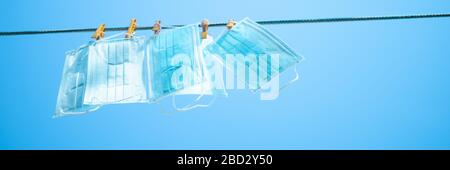 Blaue medizinische Masken hängen an einer Wäscheleine mit Wäscheklappen im blauen Himmelshintergrund. Kopierbereich. Stockfoto