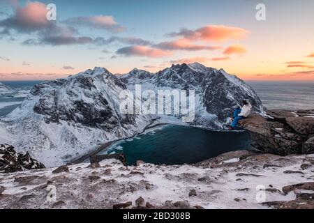 Reisende, die auf dem Ryten Berg mit Kvalvika Strand bei Sonnenuntergang auf den Lofoten Inseln, Norwegen sitzen Stockfoto