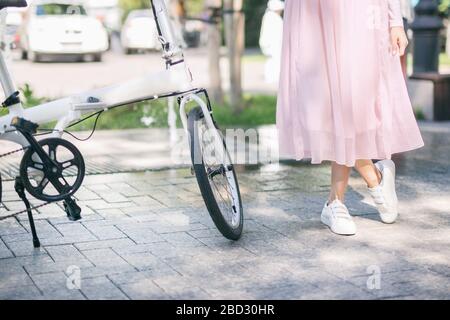 Junge Frau steht neben einem weißen Fahrrad im Park Stockfoto