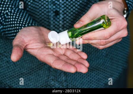 Der Mensch verwendet ein antibakterielles Händededesinfektionsmittel. Kleine Kunststoffflasche mit grüner Flüssigkeit. Handantiseptikum Stockfoto