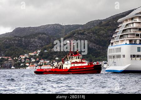 Schleppboot BB Coaster unterstützt ein großes Kreuzfahrtschiff bei der Abfahrt vom Hafen von Bergen, Norwegen. Ein regnerischer und nebeliger Tag Stockfoto