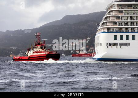 Schleppboot BB Coaster unterstützt ein großes Kreuzfahrtschiff bei der Abfahrt vom Hafen von Bergen, Norwegen. Ein regnerischer und nebeliger Tag Stockfoto