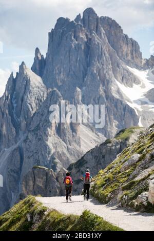 Ein paar Wanderer gehen auf einem Feldweg, mit einem felsigen Berg im Hintergrund, an einem sonnigen Sommertag Stockfoto