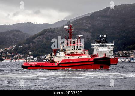 Schleppboot BB Coaster unterstützt ein großes Kreuzfahrtschiff bei der Abfahrt vom Hafen von Bergen, Norwegen. Ein regnerischer und nebeliger Tag, PSV Vessel Siem stolz auf Backgroun Stockfoto