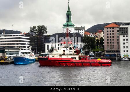 Schleppboot BB Arbeiter im Hafen von Bergen, Norwegen. Ein regnerischer und regnerischer Tag, Angelschiff Skagoeysund und Nykirken Kirche im Hintergrund Stockfoto