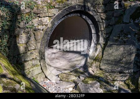 Abwasserkanal mit großer Öffnung und Steinmauer Stockfoto