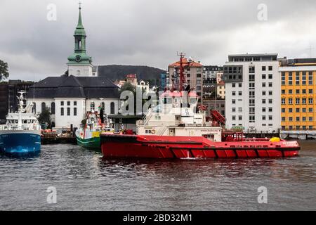 Schleppboot BB Arbeiter im Hafen von Bergen, Norwegen. Ein regnerischer und regnerischer Tag, Angelschiff Skagoeysund, Tauchschiff Octopus und Nykirken Kirche in BA Stockfoto