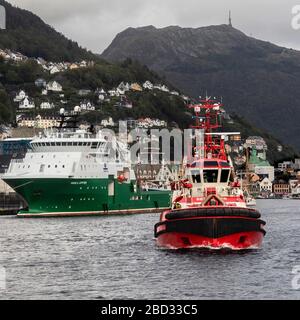 Schleppboot BB Coaster, Abfahrt vom Hafen von Bergen, Norwegen. Offshore-Versorgungsschiff Havila Jupiter und Mount Ulriken im Hintergrund Stockfoto