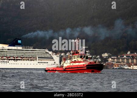 Kreuzfahrtschiff Norwegian Spirit, Abfahrt vom Bontelabo Kai im Hafen von Bergen, Norwegen. Ein grauer und regnerischer Tag. Schleppboot BB Coaster hat gerade Assist absolviert Stockfoto