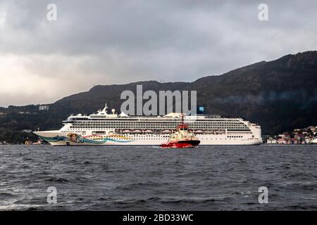 Kreuzfahrtschiff Norwegian Spirit, Abfahrt vom Bontelabo Kai im Hafen von Bergen, Norwegen. Ein grauer und regnerischer Tag. Schleppboot BB Arbeiter hat gerade Assisti abgeschlossen Stockfoto