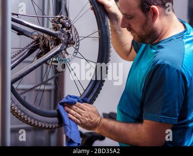 Mechaniker in einer Fahrradreparaturwerkstatt Ölen der Kette von einem Fahrrad. Mann sein Fahrrad für die neue Saison beibehalten. Arbeitsprozess. Stockfoto