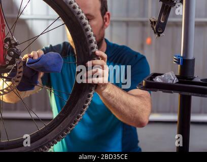 Mechaniker in einer Fahrradreparaturwerkstatt Ölen der Kette von einem Fahrrad. Mann sein Fahrrad für die neue Saison beibehalten. Arbeitsprozess. Stockfoto