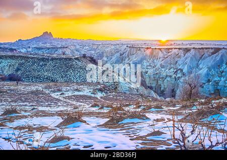 Der malerische Sonnenuntergang über dem Winter Kappadokien - heller feuriger Himmel mit Silhouette der Uchisar-Felsenburg am Horizont und Tuff-Canyon des Love Valley in den Abenddämmerung Stockfoto