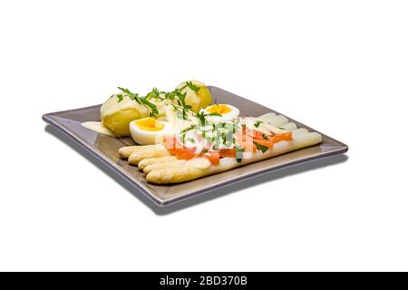 Köstlicher saisonaler weißer Spargel mit cremiger hollandaise Sauce, Baby-Kochkartoffeln und in Scheiben geschnittenem Räucherlachs auf einer rustikalen Platte mit Zitrone, weißem Wi Stockfoto