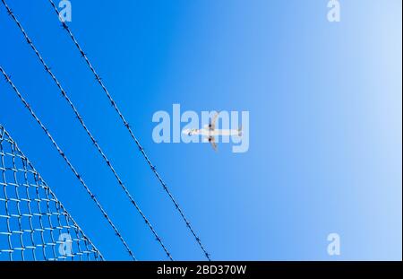 Zaun mit Stacheldraht und Ebenensilhouette auf blauem Himmelshintergrund. Stockfoto