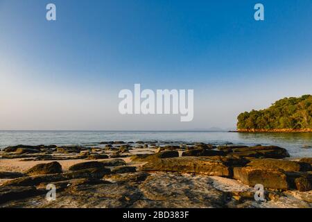 Landschaft mit Steinen, flachem Meer und Himmel. Wunderschöner Blick auf die Natur ohne Menschen, Wasseroberfläche, Horizont, Sonnenuntergang, Himmel und Grat aus flachen Steinen Stockfoto
