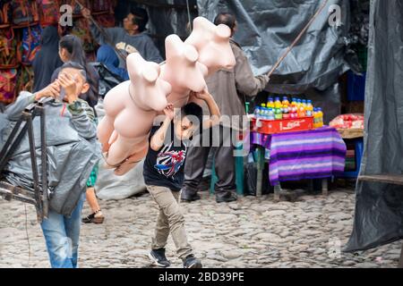 Der Junge trägt Mannequins zum Stall seiner Familie auf dem Markt von Chichicastenango, Guatemala.