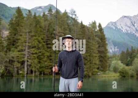 Mann, der auf dem Pier in einem schönen See und Wald mit Bergen fischt. Stockfoto