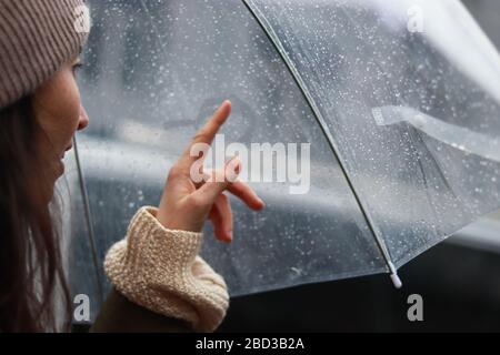 Mädchen malt das Herz auf einer nebligen Oberfläche im Regen unter einem Regenschirm. Love Story Konzept Stockfoto