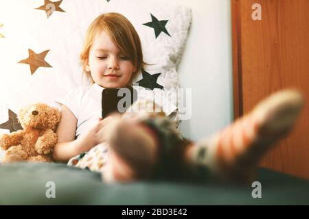 Süßes kleines lächelndes Mädchen mit Smartphone in den Händen. Konzept des Video-Chats, der Videowiedergabe oder des Spielens von Spielen. Stockfoto