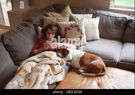 Tween Mädchen, das auf ihr Telefon schaut, während sie mit Hund auf der Couch kuscheln Stockfoto