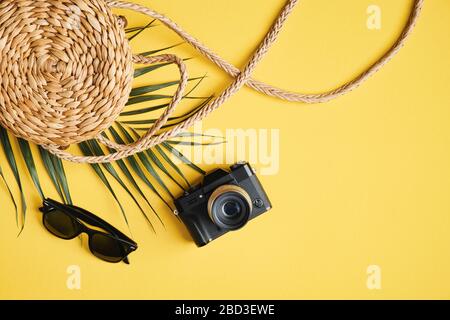 Shirt View elegantes Accessoire für Reisende von Frauen auf gelbem Hintergrund. Flache Rattantasche, Palmblatt, Sonnenbrille und Kamera. Sommerurlaub, Reisen, Urlaub Stockfoto