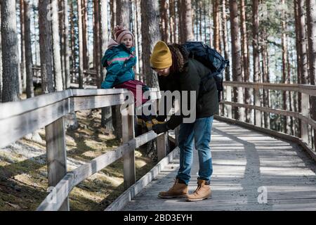 Vater hilft seiner Tochter, ihren Schuh zu ziehen, während sie im Wald läuft Stockfoto