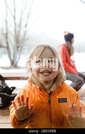 Breite Augen lächelnd 3-jährige Mädchen schaut durch Fensterscheibe auf Onkel Stockfoto