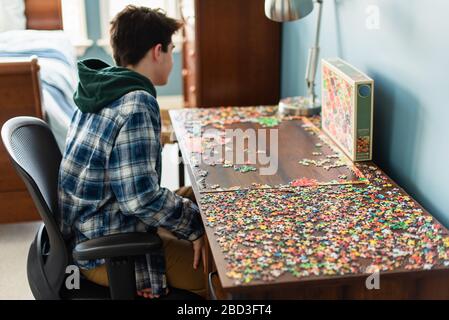 Teen Junge arbeitet an einem Puzzle in seinem Schlafzimmer während Covid 19. Stockfoto