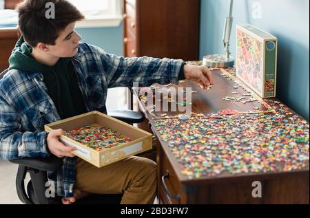 Teen Junge arbeitet an einem Puzzle in seinem Schlafzimmer während Covid 19. Stockfoto