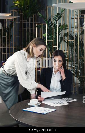Zwei Geschäftsfrauen schütteln die Hände in der Nähe eines Schreibtischs, während sie ein Geschäft oder eine Partnerschaft schließen Stockfoto