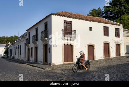 Kolonialhaus an der Ecke am Hafen mit Mädchen auf einem Motorrad in Colonia del Sacramento, Uruguay. Stockfoto