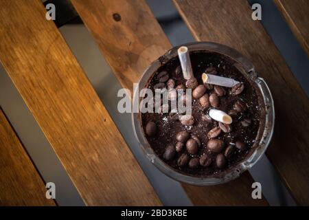 Zigarette in Glasaschenbecher auf Holztisch. Stockfoto