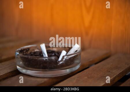 Zigarette in Glasaschenbecher auf Holztisch. Stockfoto